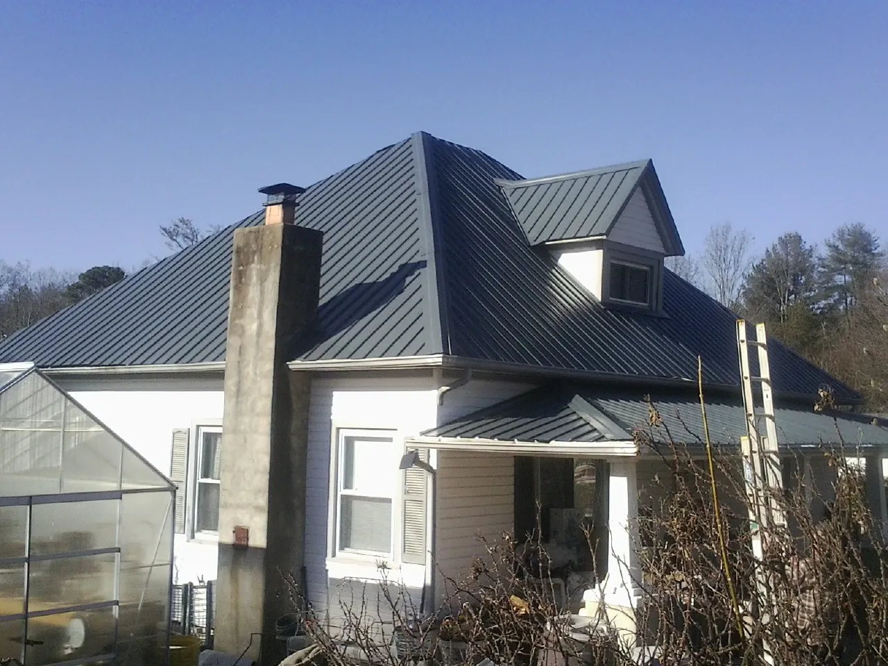 Dark blue standing seam metal roof on a white farmhouse with dormer — Slate & Tile Roof Repair by Roofing Brothers in Ronald