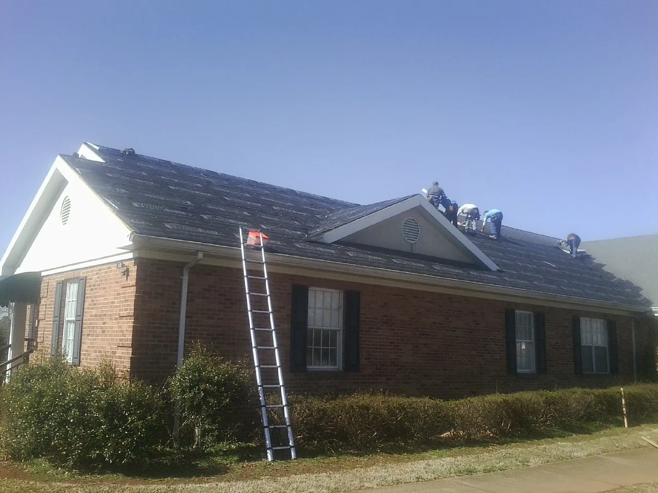 Crew tearing shingles off a brick ranch roof with a ladder set — Emergency Roof Repair work by our crew in Ronald