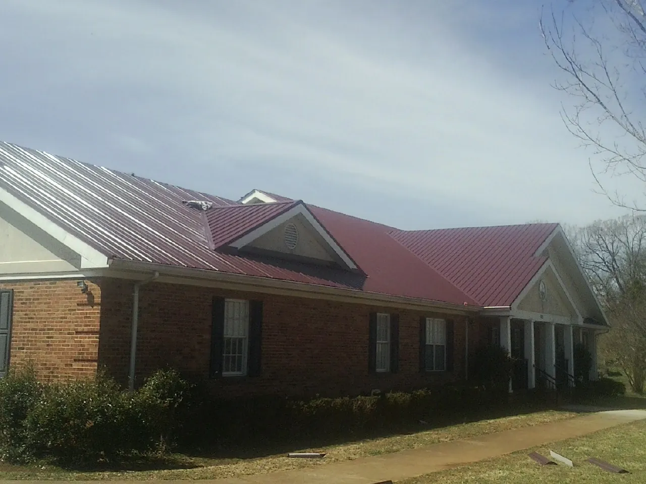 Red metal roof with gabled entries on a long brick building, from a Hail Damage Roof Repair job in Ronald