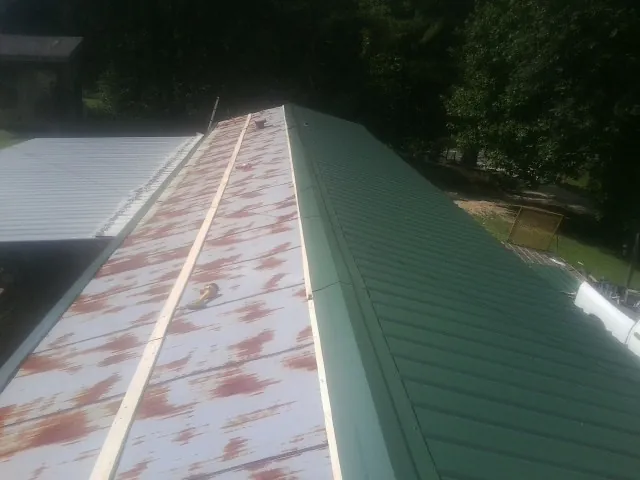 Old rusted panels beside newly installed green metal roofing — Wind Damage Roof Repair by Roofing Brothers in Ronald