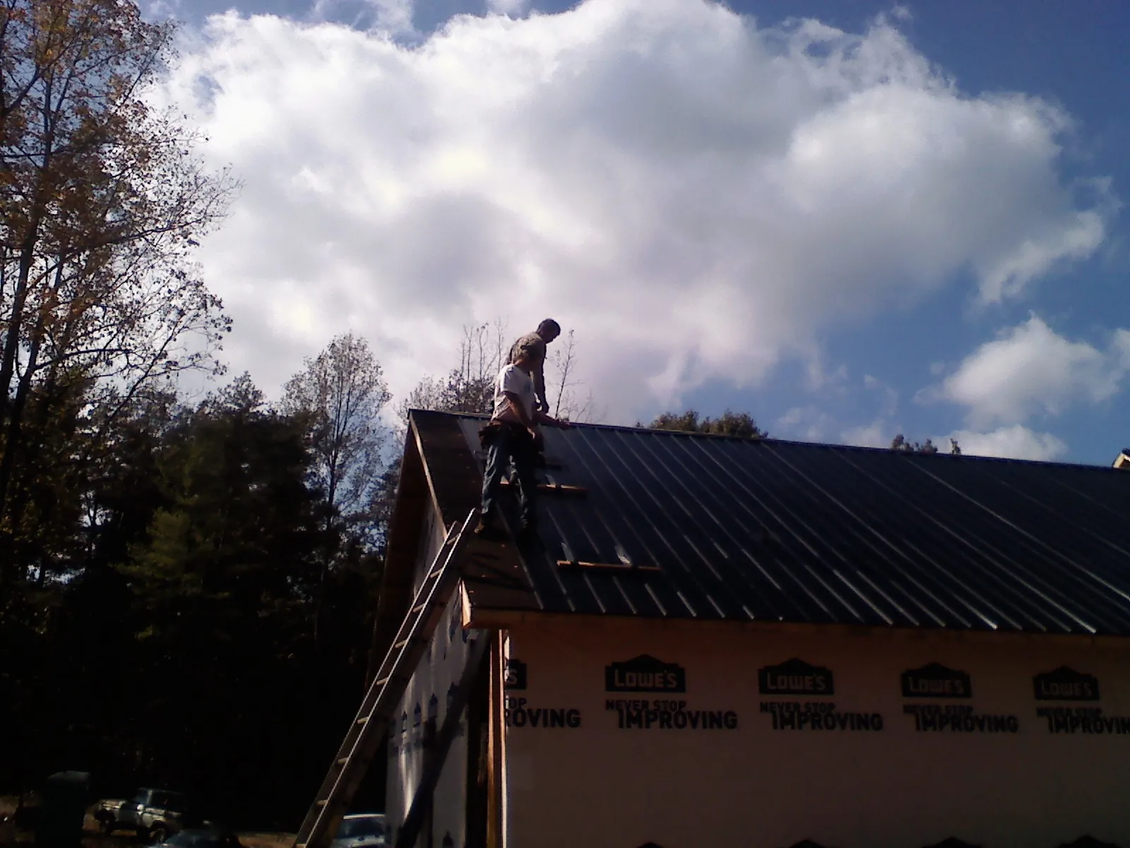 Roofer fastening dark metal panels high against a cloudy sky, from a Roof Inspection job in Ronald