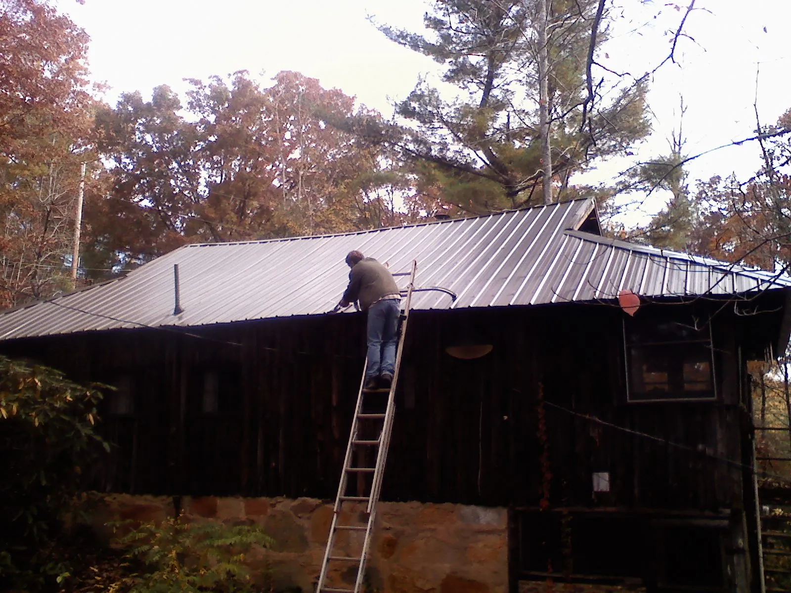 Roofer on a ladder working along the edge of a cabin metal roof in Ronald