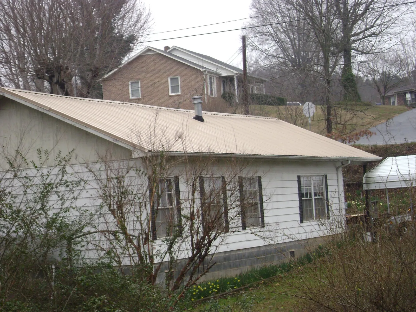 Tan metal roof on a white sided house set into a hillside — Commercial Roofing by Roofing Brothers in Ronald