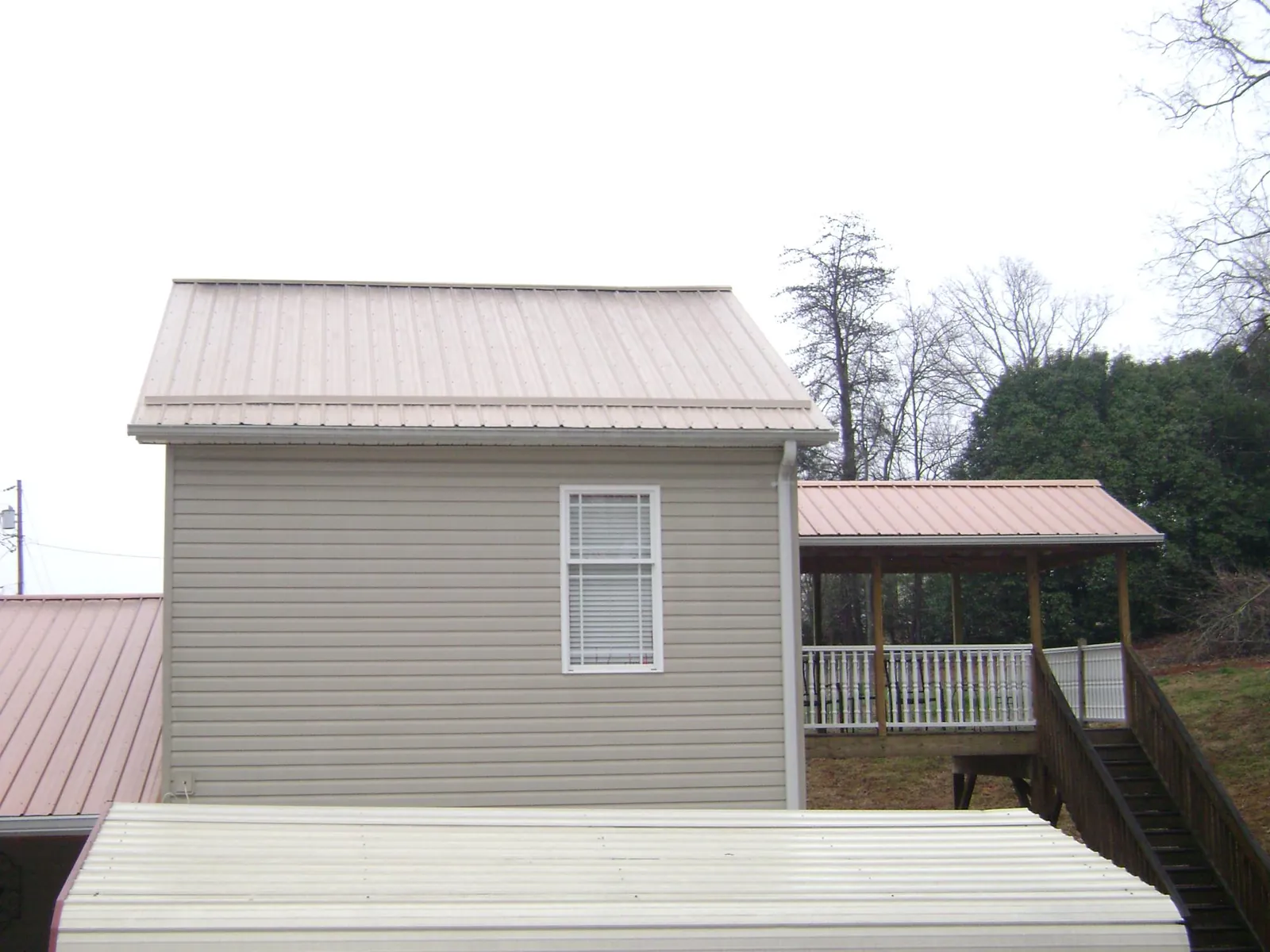 Tan metal roofs on a two story addition and attached porch, from a Roof Replacement job in Ronald